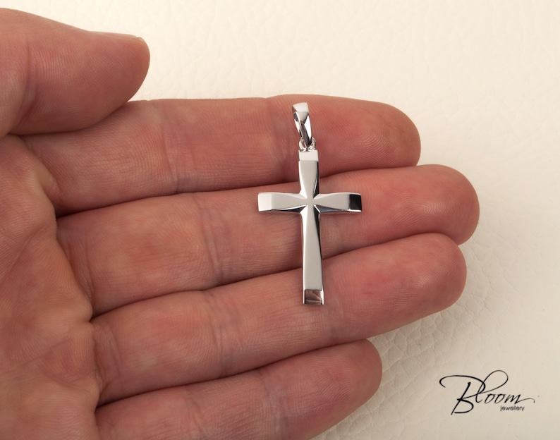 K&ouml;nnte beinhalten: Ein silberner Kreuzanh&auml;nger mit einem schlichten, geometrischen Design. Das Kreuz wird in einer Hand gehalten, wodurch seine Gr&ouml;&szlig;e und Details hervorgehoben werden.