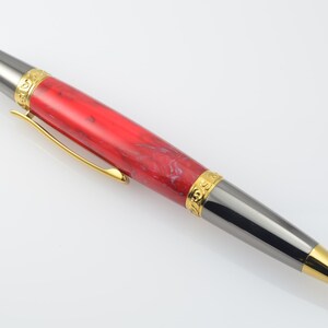 May include: A red and black pen with gold accents. The pen has a marbled red and white barrel and a black metal tip with a gold band.
