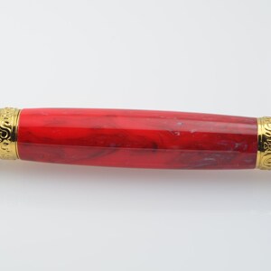May include: A red and black pen with gold accents. The pen has a marbled red design and gold trim around the ends.