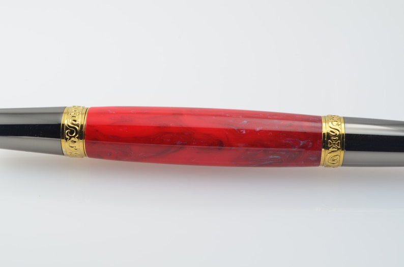 May include: A red and black pen with gold accents. The pen has a marbled red design and gold trim around the ends.