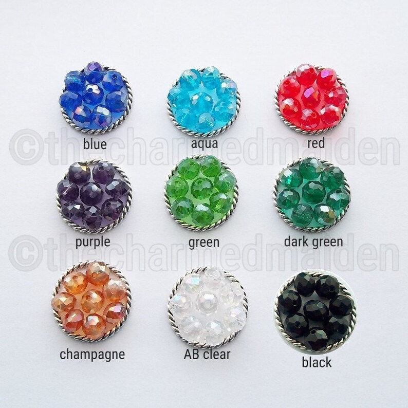 May include: Nine round, beaded buttons in various colors, including blue, aqua, red, purple, green, dark green, champagne, AB clear, and black. Each button has a silver-colored rope-like border and the color name printed below.