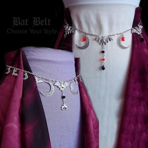 May include: Two silver bat belt chains with crescent moon and bat charms. The chain on the left has black and red beads, while the chain on the right has red and black beads. The text "Bat Belt Choose Your Style" is visible at the top of the image.