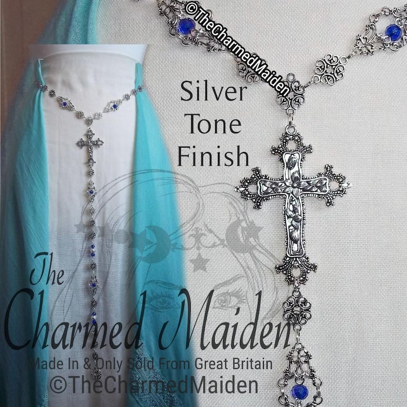 May include: Silver-tone necklace with a cross pendant and blue accents. The necklace features intricate filigree detailing and is displayed against a light blue and white background. The text "The Charmed Maiden" is visible.
