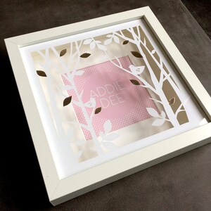 May include: White frame with a white paper cutout design of trees and leaves. The cutout design is layered over a pink background with white polka dots. The text "ADDIE DEE" is in gold lettering on the pink background.