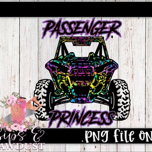 May include: A colourful graphic design of a side-by-side off-road vehicle with the words "Passenger Princess" above and below the vehicle. The design is on a white wood background.