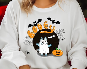 May include: White long-sleeved shirt with a black and orange Halloween-themed graphic. The graphic features a ghost cat with the word "Booey" in orange letters.