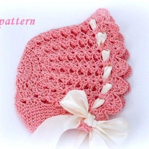 May include: A pink crocheted bonnet with a scalloped edge and ivory satin ribbon ties. The bonnet features an openwork design and the word "pattern" in pink script. A delicate, handmade baby accessory.
