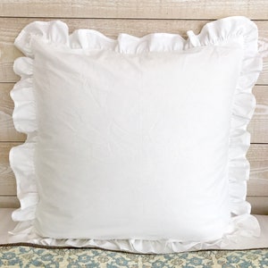 May include: A square white pillow with ruffled edges. The pillow is made of a soft, textured fabric and has a simple, elegant design. The ruffled edges add a touch of sophistication to the pillow.