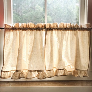May include: Two beige ruffled curtains hang in a window with a wooden frame. The curtains are held up by a black rod. The curtains are made of a light, airy fabric.