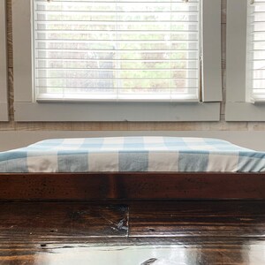 May include: A wooden dog bed frame with a blue and white checkered cushion. The bed is sitting on a dark wood floor.