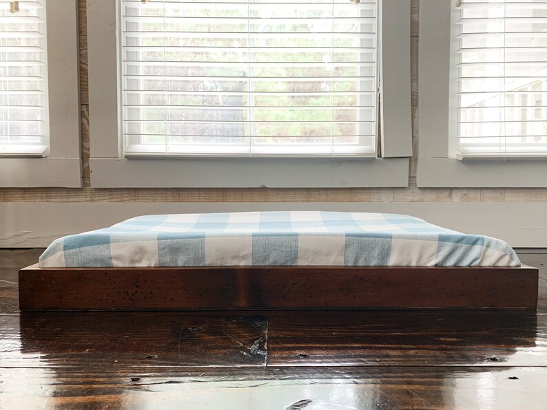 May include: A wooden dog bed frame with a blue and white checkered cushion. The bed is sitting on a dark wood floor.