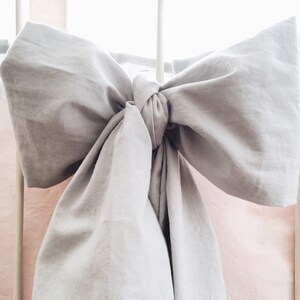 May include: A gray fabric bow tied around a white crib rail with a pink and white fabric background.