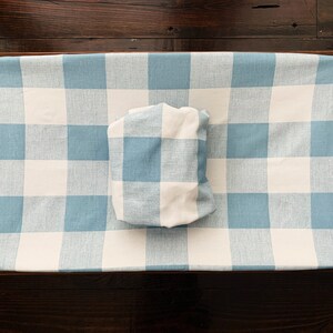 May include: A blue and white checkered changing pad cover with a matching pillow. The cover is made of a soft, woven fabric.
