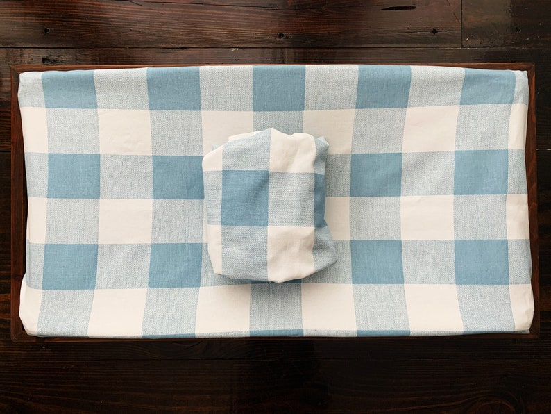 May include: A blue and white checkered changing pad cover with a matching pillow. The cover is made of a soft, woven fabric.