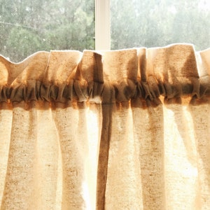 May include: A pair of off-white cotton cafe curtains with a gathered top and a simple, rustic look.