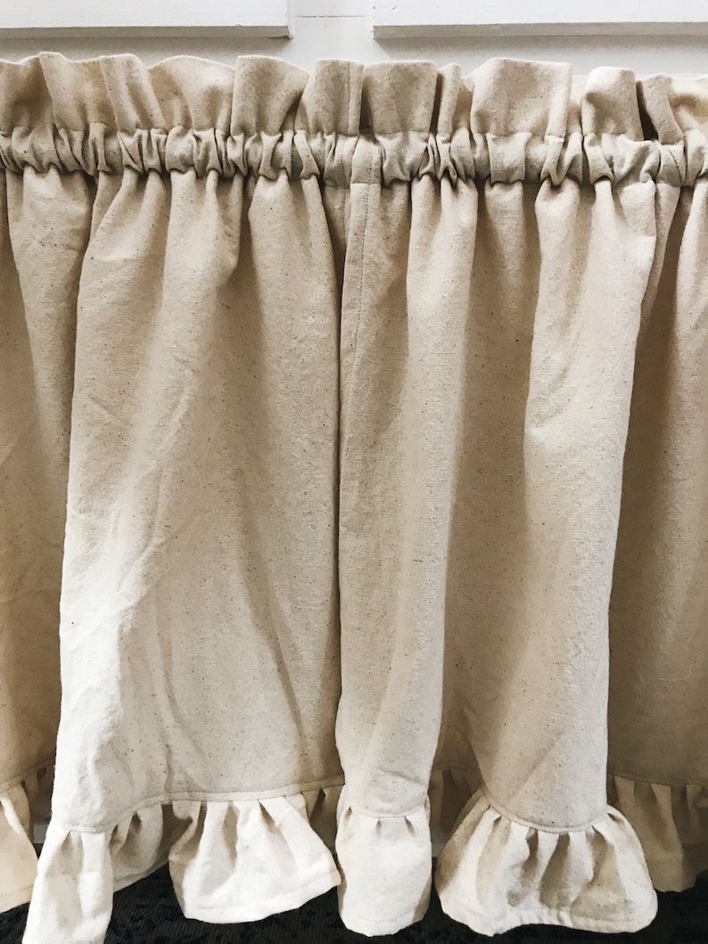 May include: A pair of off-white, ruffled curtains with a gathered top. The curtains are made of a lightweight, textured fabric.