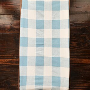 May include: A blue and white gingham changing pad cover. The cover is made of a soft, breathable fabric and is perfect for keeping your baby's changing area clean and stylish.
