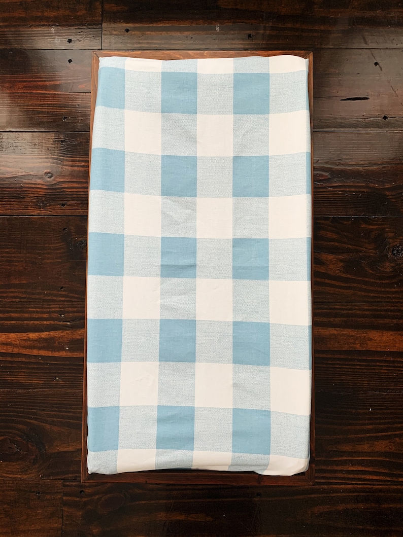 May include: A blue and white gingham changing pad cover. The cover is made of a soft, breathable fabric and is perfect for keeping your baby's changing area clean and stylish.