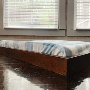 May include: A wooden platform bed frame with a blue and white checkered mattress pad. The frame is made of dark wood and has a simple, modern design.