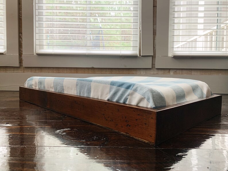 May include: A wooden platform bed frame with a blue and white checkered mattress pad. The frame is made of dark wood and has a simple, modern design.