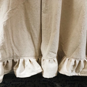 May include: Close-up of a pair of off-white curtains with a ruffled hem. The curtains are made of a textured fabric and have a subtle sheen.