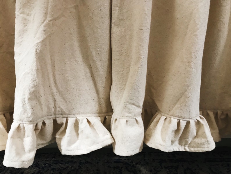 May include: Close-up of a pair of off-white curtains with a ruffled hem. The curtains are made of a textured fabric and have a subtle sheen.