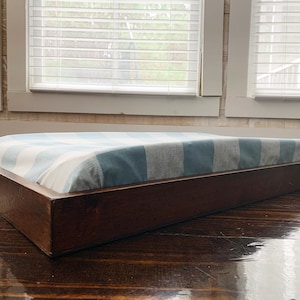 May include: A wooden dog bed with a blue and white striped cushion. The bed is sitting on a wooden floor.