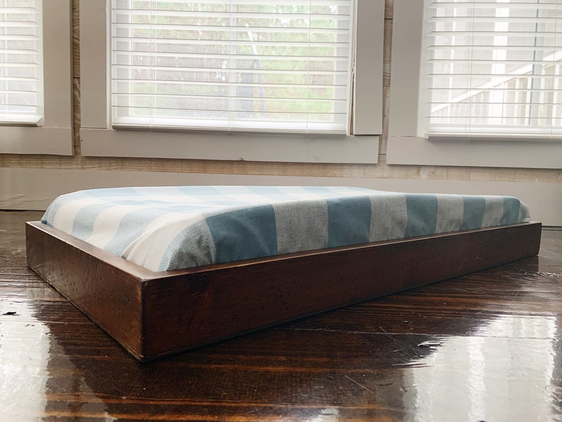 May include: A wooden dog bed with a blue and white striped cushion. The bed is sitting on a wooden floor.
