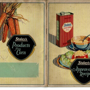 May include: A vintage cookbook cover with a yellow background and a black and gold logo that says "Staley's Products from Corn". The left side of the cover features a drawing of corn on the cob. The right side of the cover features a drawing of a can of Staley's Salad and Cooking Oil, a bowl of salad dressing, and a salad with a black and gold logo that says "Staley's Approved Recipes".