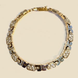 May include: A circular link bracelet featuring alternating gold-tone metal segments and silver-tone metal segments. The gold-tone segments are embellished with small, clear, round-cut stones set in a cluster pattern. The bracelet includes a metal clasp.