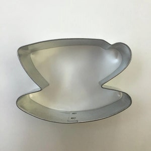 May include: A silver metal cookie cutter shaped like a teacup and saucer.