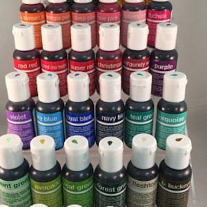 May include: A set of 30 small bottles of food coloring in various colors, including red, blue, green, purple, and yellow. The bottles are arranged in rows on a white surface.