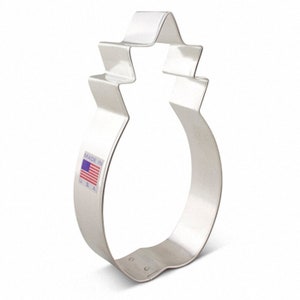 May include: A silver metal pineapple cookie cutter with a detailed design. The cutter has a "Made in USA" label on the side.