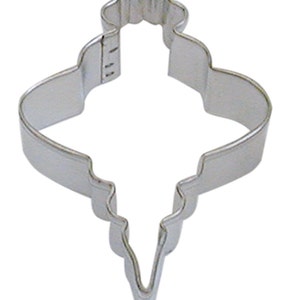 May include: A silver metal cookie cutter shaped like a Christmas ornament. The ornament has a pointed bottom and a rounded top with a scalloped edge.