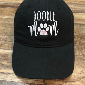 Op de afbeelding: Zwarte baseballpet met witte borduurwerk die "Doodle Mom" met een roze pootprint zegt.