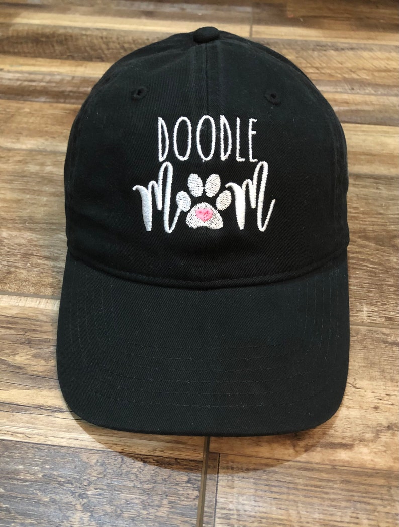 Op de afbeelding: Zwarte baseballpet met witte borduurwerk die "Doodle Mom" met een roze pootprint zegt.
