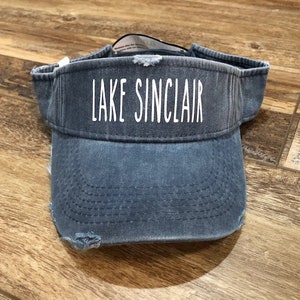 May include: A blue denim visor with a distressed look and white text that reads "LAKE SINCLAIR".