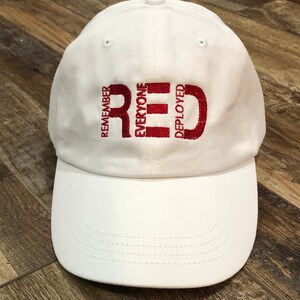 May include: White baseball cap with red embroidered text that reads "Remember Everyone Deployed Red".