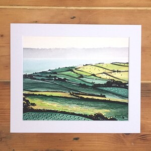May include: A watercolour painting of a landscape with rolling green hills and a body of water in the distance. The sky is a light blue with a few clouds.