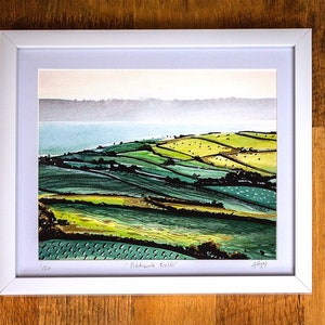 May include: A framed watercolour painting of a green and yellow landscape with a body of water in the background. The painting is titled "Patchwork Fields" and is signed by the artist.