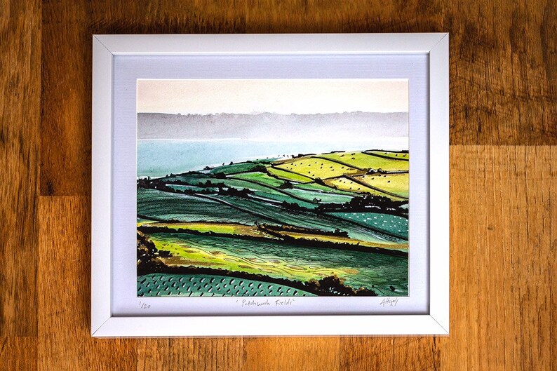 May include: A framed watercolour painting of a green and yellow landscape with a body of water in the background. The painting is titled "Patchwork Fields" and is signed by the artist.