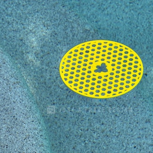 May include: A bright yellow, oval-shaped object with a honeycomb pattern floats in clear, blue water. The object has a small, flower-like design in the center. The water has a textured, speckled appearance.