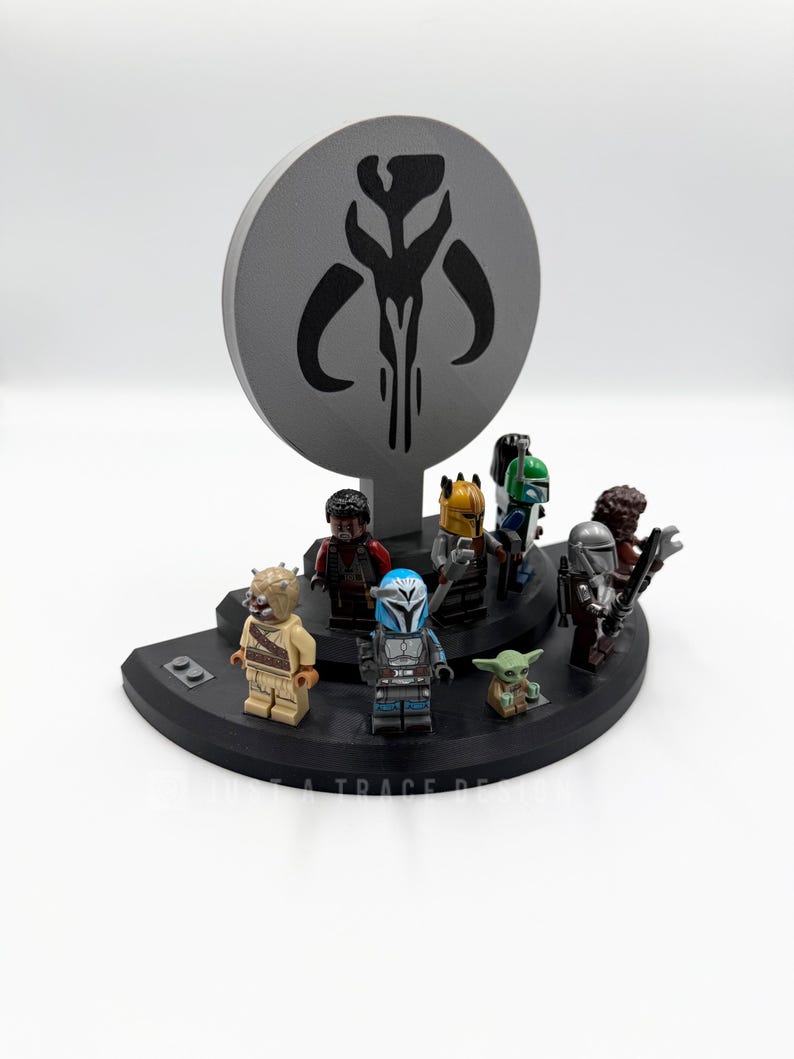 May include: A black display stand featuring several Star Wars Lego minifigures, including The Mandalorian and Grogu. A gray circular backdrop displays a Mandalorian symbol. The stand is on a white surface.