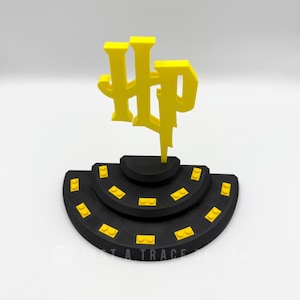 May include: A black and yellow 3D-printed display stand featuring the Harry Potter logo. The logo is in yellow and is mounted on a tiered, semi-circular black base with yellow accents. The design is set against a white background.