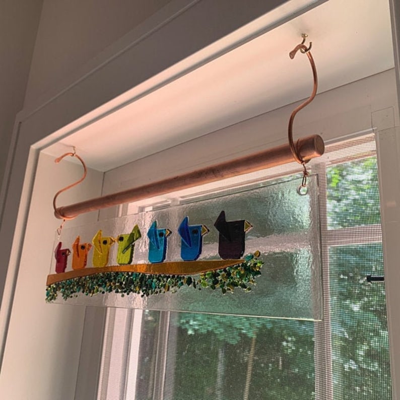 Peut inclure: Une fen&ecirc;tre en verre color&eacute; suspendue &agrave; une tige et des crochets en cuivre. Le vitrail repr&eacute;sente une rang&eacute;e d'oiseaux color&eacute;s perch&eacute;s sur une branche avec des feuilles vertes.