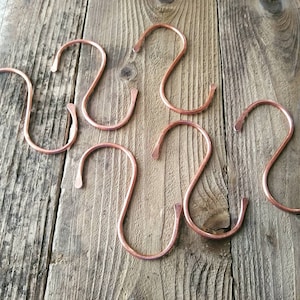 May include: Six copper S-shaped hooks on a wooden surface. The hooks are a warm copper color and have a smooth, polished finish.