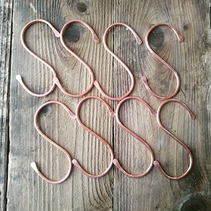 May include: A set of eight copper S-shaped hooks. The hooks are arranged in two rows of four, with the hooks in each row alternating directions.