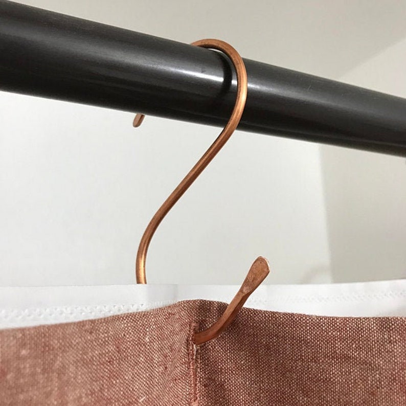 Peut inclure: Un crochet en forme de S de couleur cuivre est suspendu &agrave; une barre en m&eacute;tal noir. Le crochet est fix&eacute; &agrave; un rideau en tissu brun.