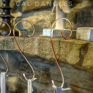 May include: Three copper stocking holders with a decorative swirl design. The holders are mounted on a stone fireplace mantel.
