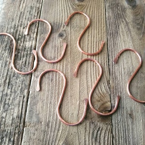 Peut inclure: Six crochets en forme de S en cuivre sur une surface en bois. Les crochets sont de couleur cuivre chaud et ont une finition lisse et polie.